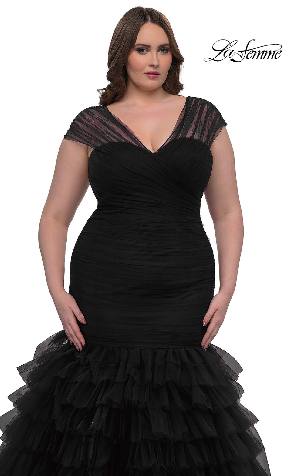 A woman models the Plus-Size Long Mermaid Prom Dress La Femme 32389, featuring fitted black cap sleeves, sheer details, and a ruffled skirt, standing against a white background with the La Femme logo in the top right corner.